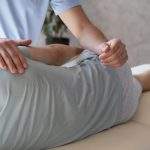 Close-up of a physiotherapist wearing a medical mask gently assisting a patient by supporting and guiding their leg during a physical therapy session