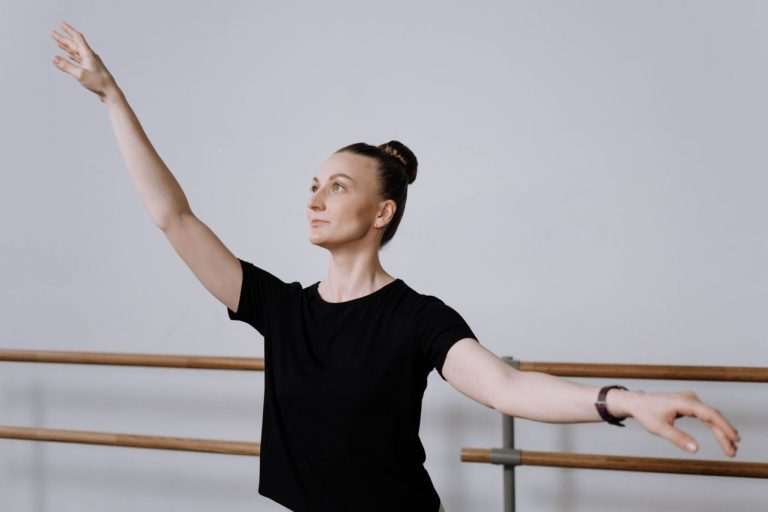 Ballet dancer in a black t-shirt practicing graceful arm positions in a dance studio.