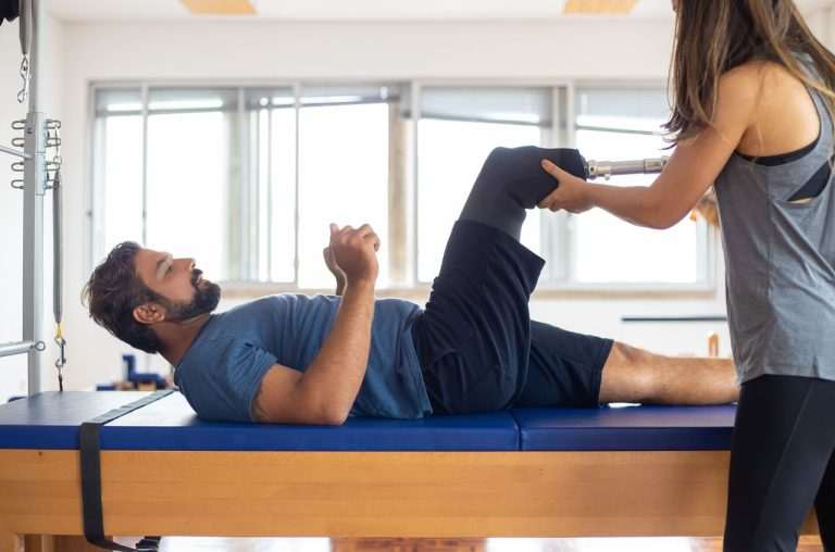A physical therapist assisting a man with a prosthetic leg during a stretching exercise.